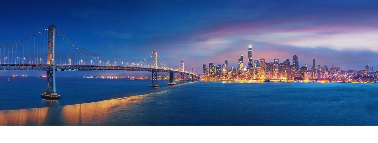 San Francisco Bay Bridge and city skyline lit up at night
